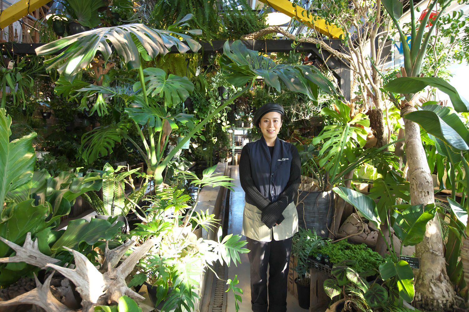 たくさんの観葉植物に囲まれて立つ笠原さん