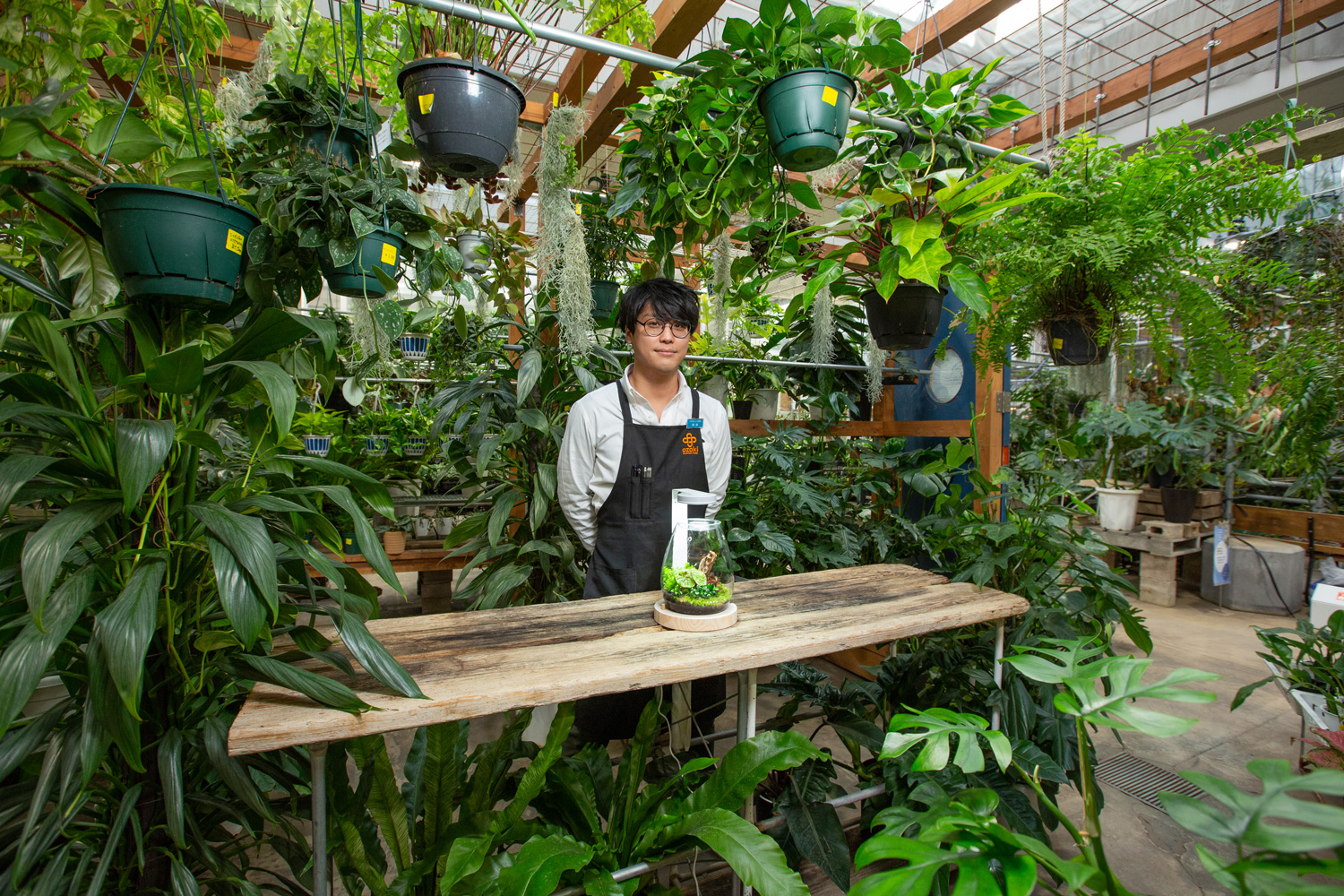 ショップに並べられた観葉植物の中に立つ鹿島さんと完成したガラスポットSHIZUKU